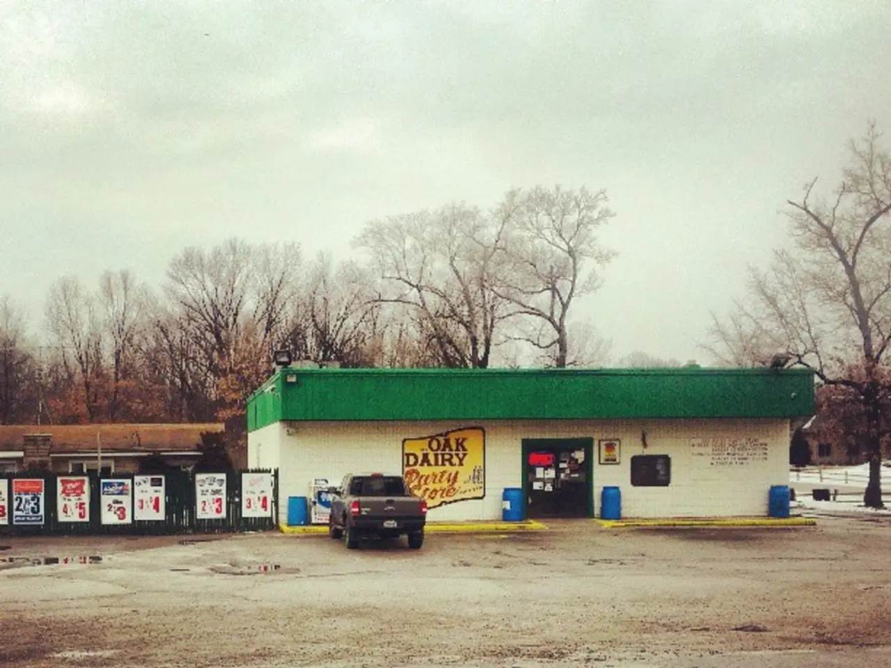 In the image there is a building in the back with a truck in front and followed by a road in the...