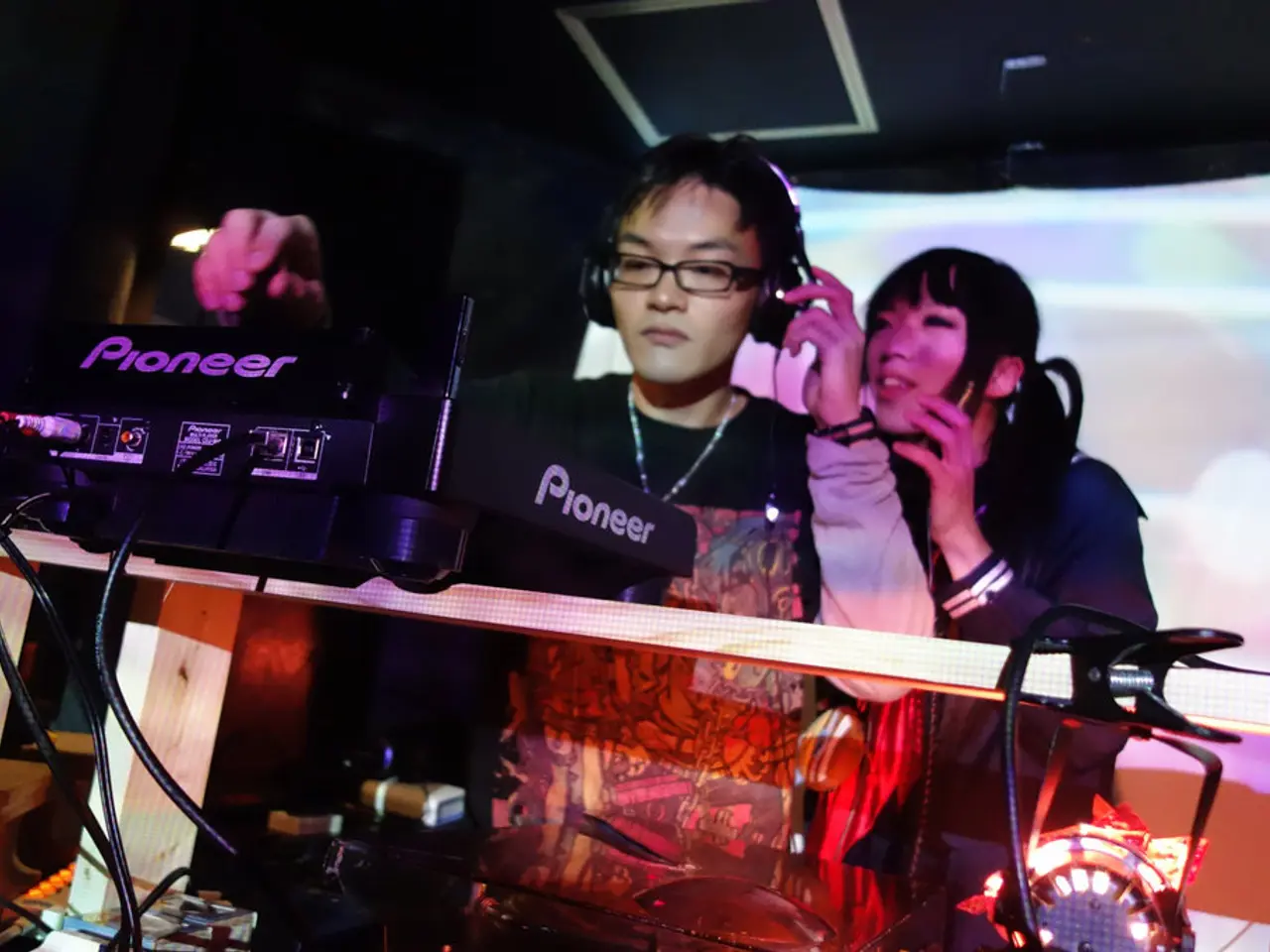 In this image there is a person wearing headphones is DJ mixing, behind the person there is a girl...