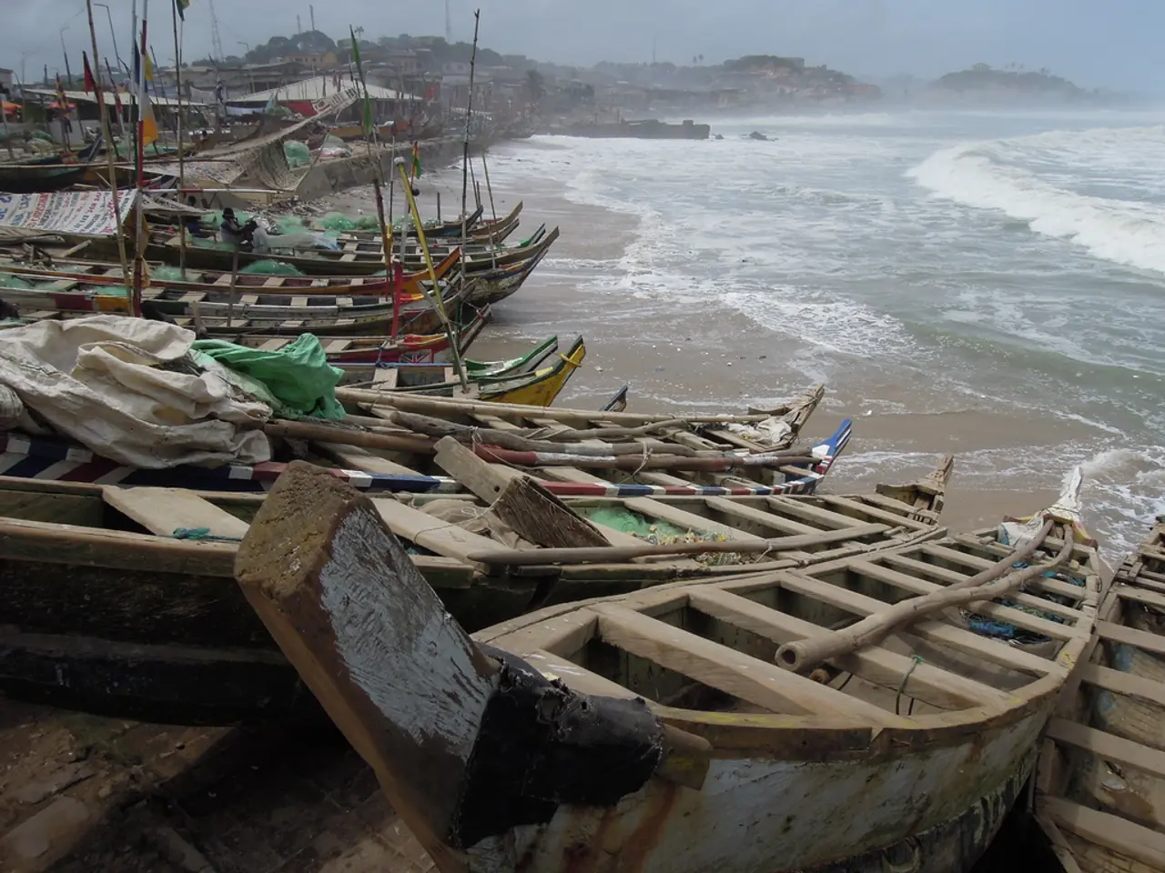 In this image I can see number of boats and few flags. I can also see water and in the background I...