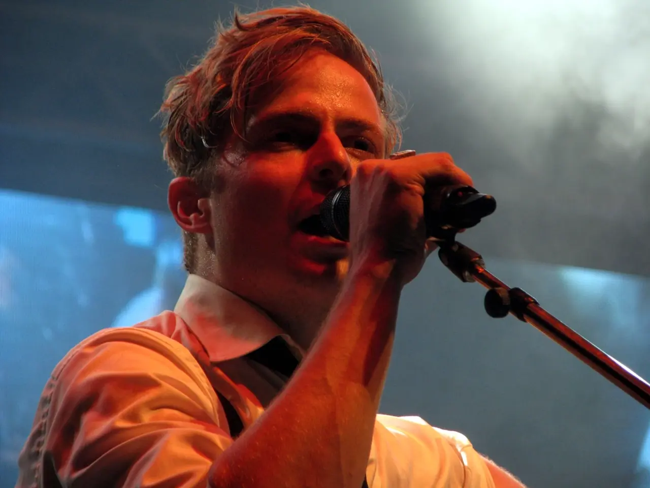 In the center of the image, we can see a man holding a mic and in the background, we can see a...