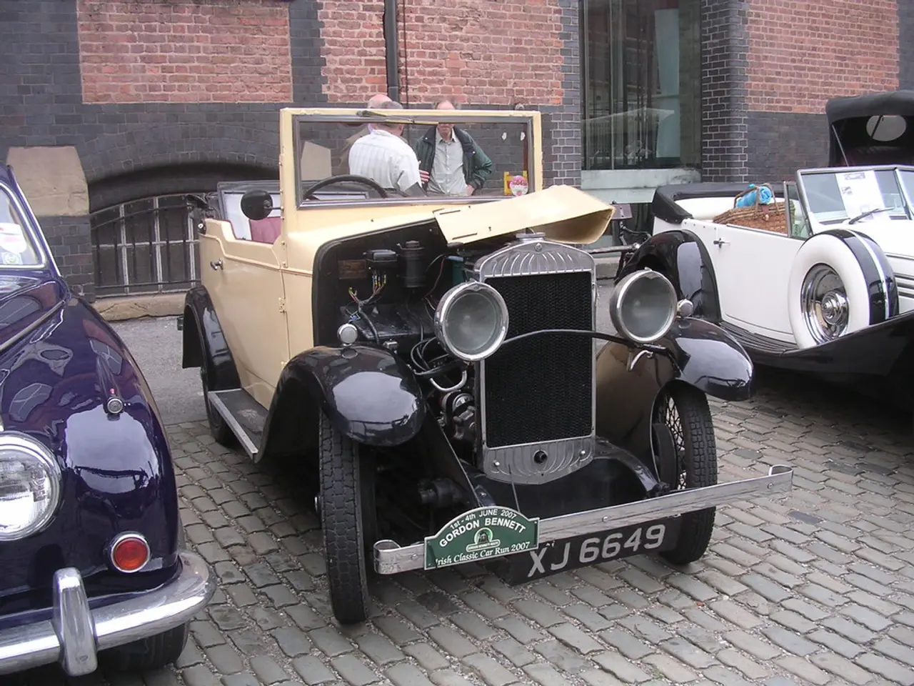 In this image in the center there are some vehicles, and in the background there are some people,...