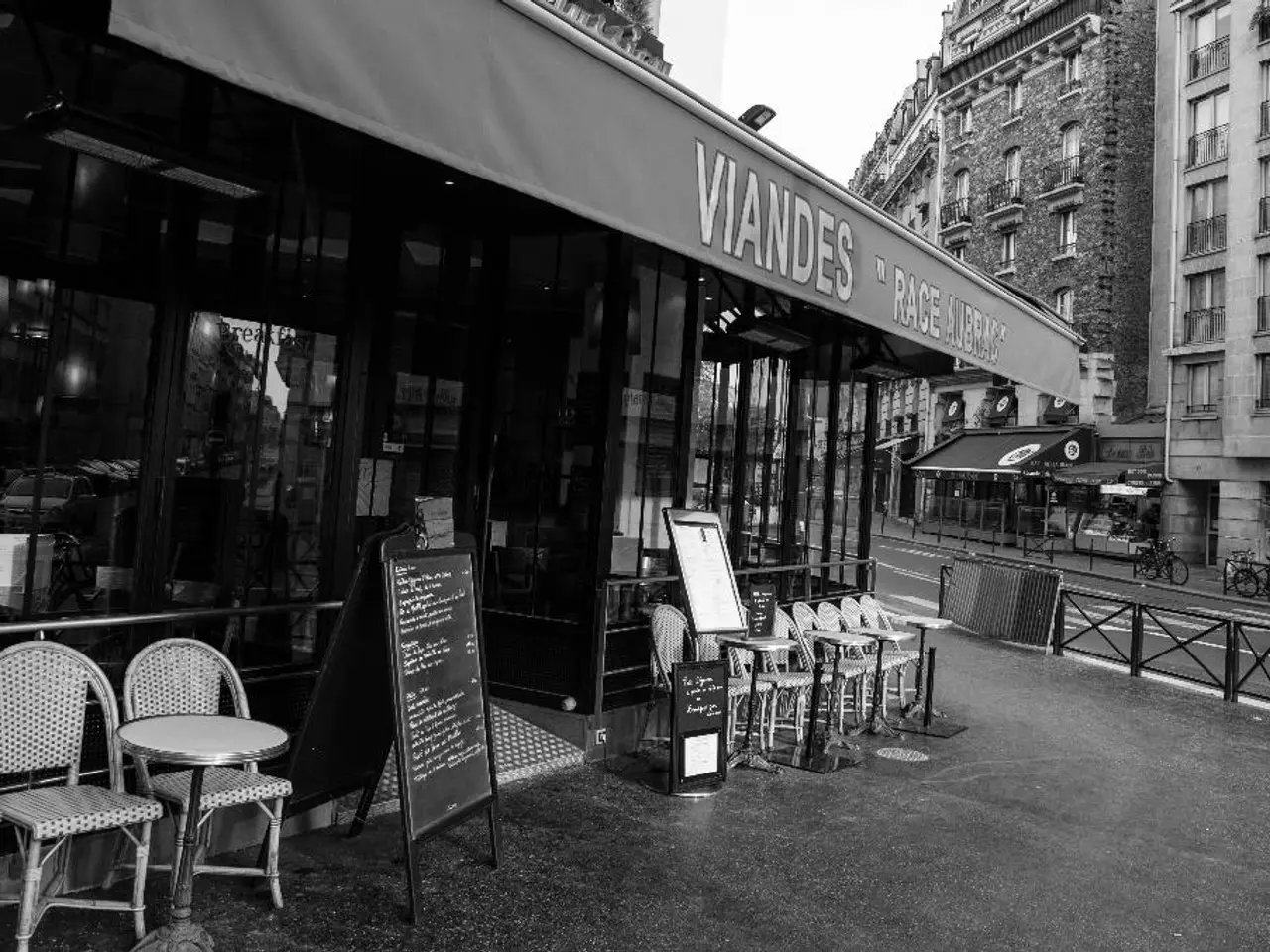 This is a black and white image. At the center of the image there is a store,There are chairs. At...