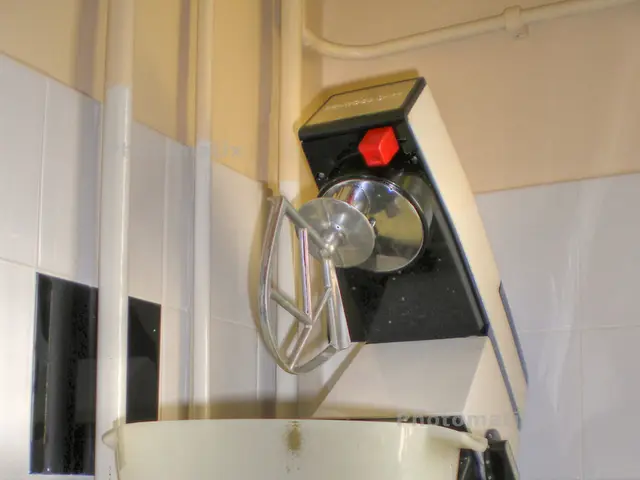 In this image we can see a machine on a platform. In the background we can see pipes and wall.