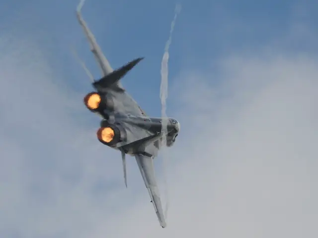 In this picture we can see an airplane in the air and smoke. In the background of the image we can...