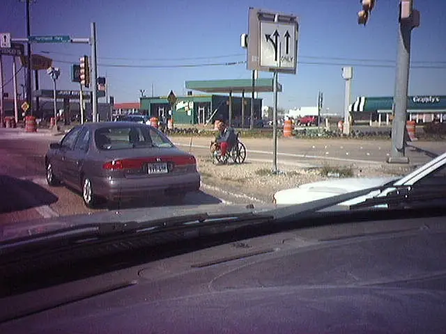 This is the picture of a car mirror from which we can see some vehicles, houses, poles which has...